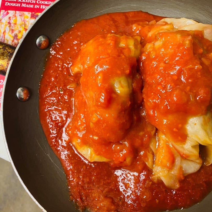 Close-up of stuffed cabbage rolls in a pan, covered in rich red tomato sauce.