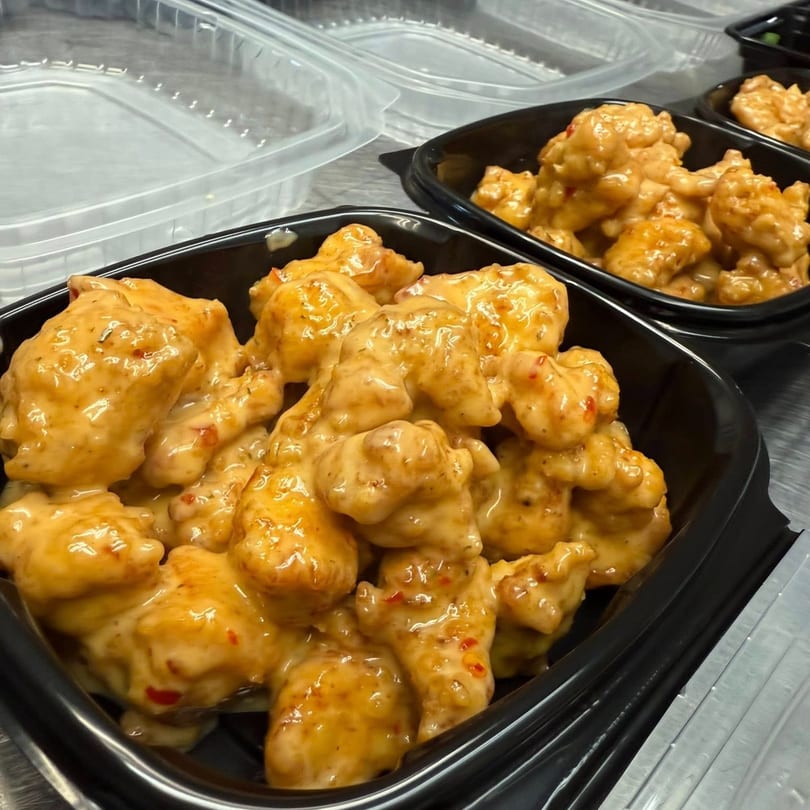 Rego's Brickhouse Pizza's boneless wings coated in a creamy orange sauce, served in black takeout containers.
