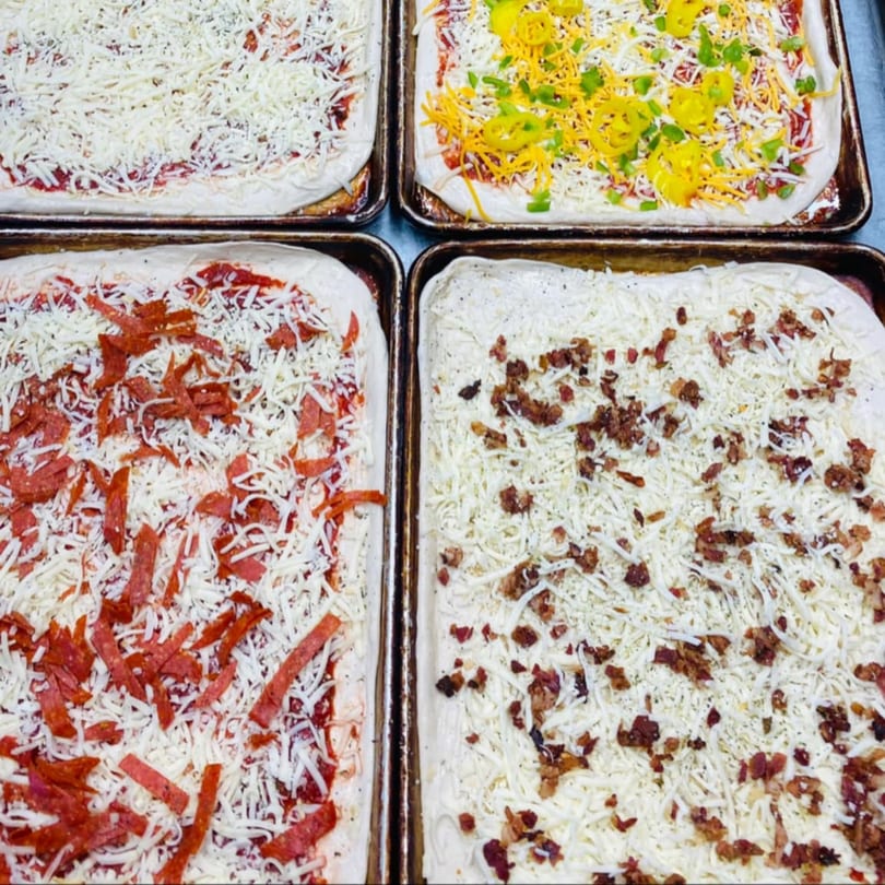 Four uncooked Rego's Brickhouse pizzas with various toppings, including pepperoni, bacon, and peppers.