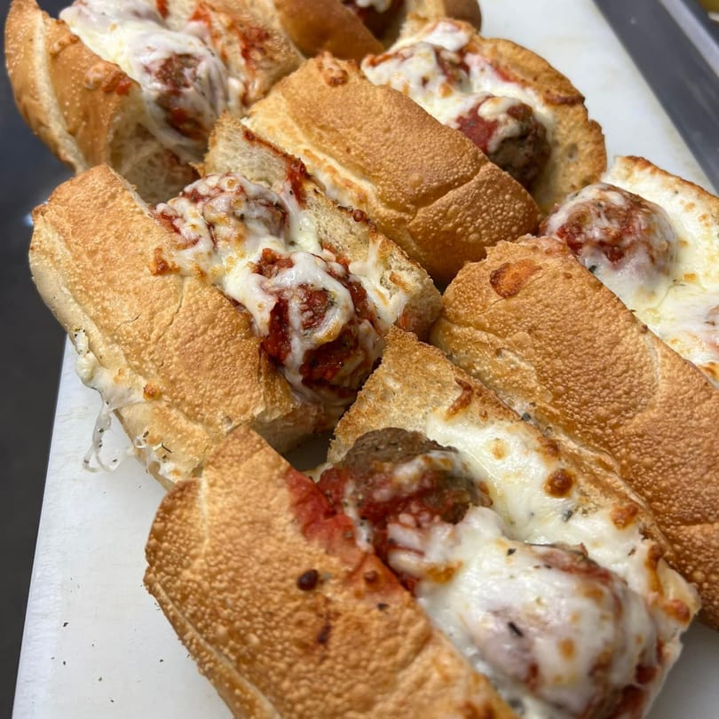 Several Rego's Brickhouse Pizza meatball subs, with melted cheese and sauce, on a white surface.