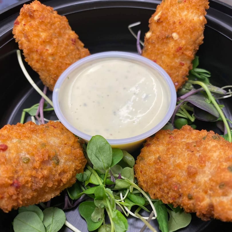 Four golden-brown fried appetizers with a side of creamy dipping sauce and fresh greens.