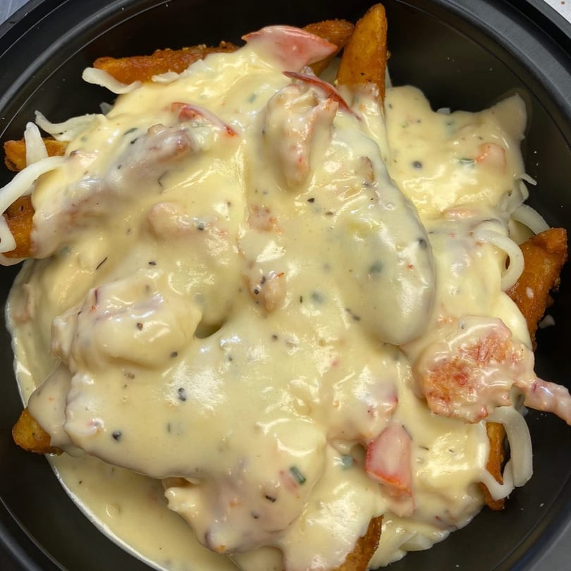 Rego's Brickhouse Pizza's cheesy fries topped with lobster and white sauce in a black bowl.