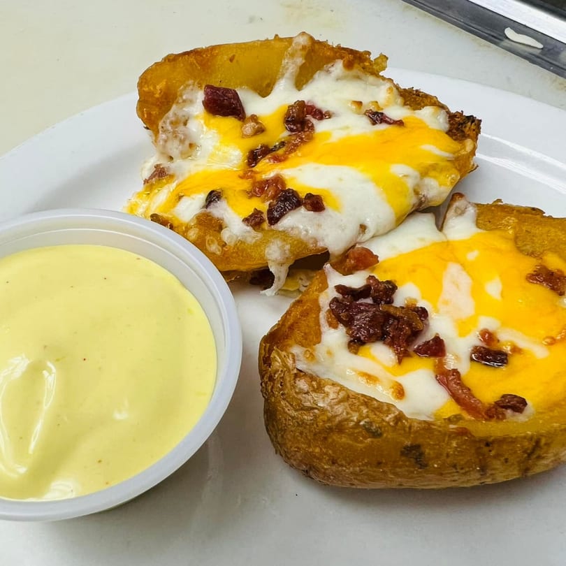 Two loaded potato skins with melted cheese and bacon bits, served with a side of dipping sauce.